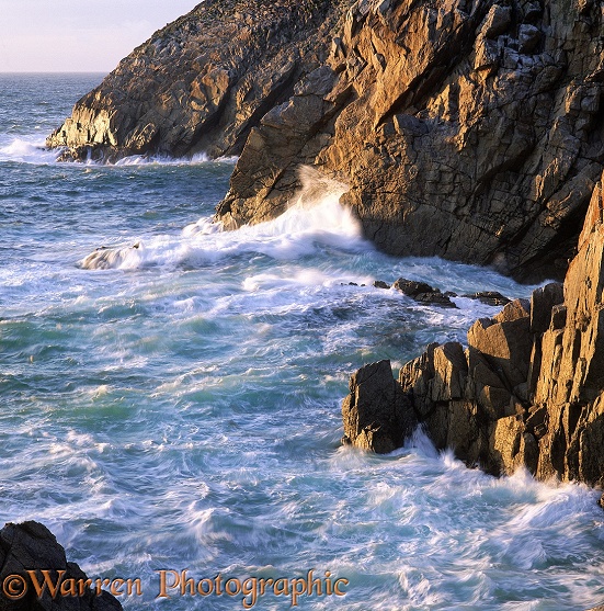 Waves breaking on a granite cliff at sunset.  Lundy Island, England
