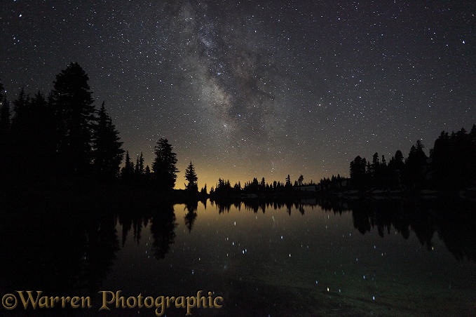 Lake with reflected stars of the Milky Way and silhouette trees.  Lassen Volcanic National Park, California