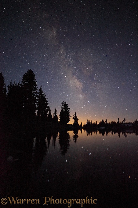 Lake with reflected stars of the Milky Way and silhouette trees.  Lassen Volcanic National Park, California