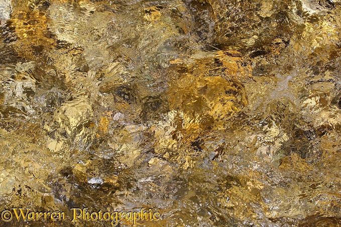 A clear stream flowing over colourful pebbles.  France