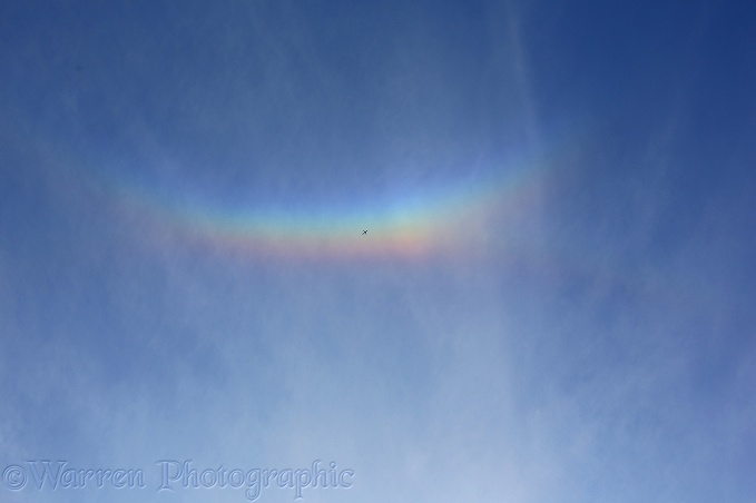 A jet liner passes beneath a 'cloudbow' caused by ice crystals in high cloud refracting light from the setting sun