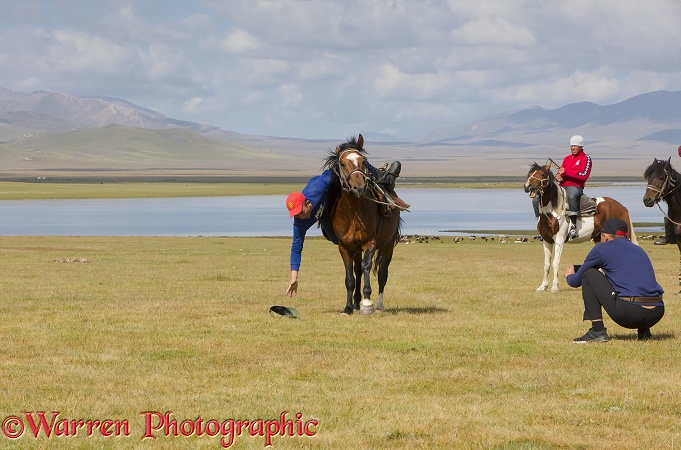Horse rider trying to pick up a hat from the ground, as he canters past.  Song Kul Lake, Kyrgyzstan