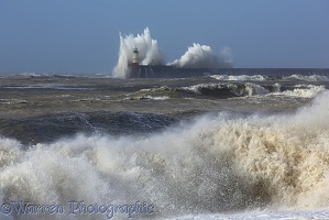 Waves breaking over lighthouse and wall